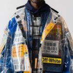 A man is wearing an oversized, transparent plastic jacket with blue and yellow J...