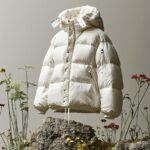 A white down jacket, hanging on moss and rocks, with a light grey and beige back...