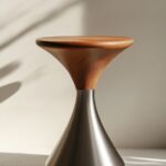 A minimalist stool with a stainless steel base and wood top, photographed in the...