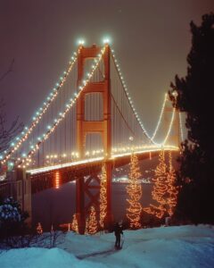 the golden gate bridge lit up at night with christmas lights. there is a person ...