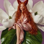 an editorial photo of a beautiful woman with fox ears sitting on a huge green ma...
