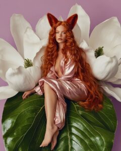 an editorial photo of a beautiful woman with fox ears sitting on a huge green ma...