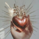 An antique hand holding the sacred heart of divine love, with silver ornaments a...