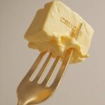 Prompt:A realistic piece of creamy butter pierced...
