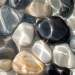 A macro image of smooth, river stones submerged beneath flowing rippling water. ...