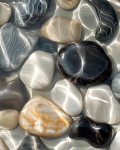 A macro image of smooth, river stones submerged beneath flowing rippling water. ...
