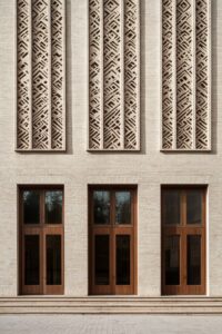 A minimalist building facade made of beige brick with large wooden windows and a...