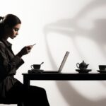 Side view of smiling woman looking at laptop on table and drinking coffee. minim...