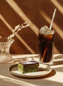 A realistic advertising photo of black ice coffee and green tea cake, in a glass...
