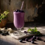 Blueberry milkshakes in a round serving glass table background , side ANGLE full...