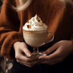 A white cup with cinnamon and whip cream is shown to be in hand, in the style of...