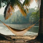 A hammock strung between two palm trees on the beach river's edge, swaying gentl...