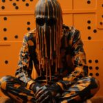 Wide fashion shot of Man wearing a futuristic mask next a bank partially covered...