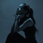 girl sits on her knees, hands under chin, long sleek ponytail hairstyle, eyes cl...