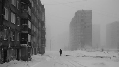 A solitary figure walks down a snowy, 1990, desolate urban street flanked by som...