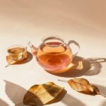 A glass teapot of wolfberry tea lies on oiled leaves and next to it is a small c...