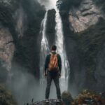 A man stands in front of a waterfall in the mountains, in the style of 32k uhd, ...