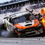 an orange, black, and white nascar violently crashing at daytona speedwayby bigm...