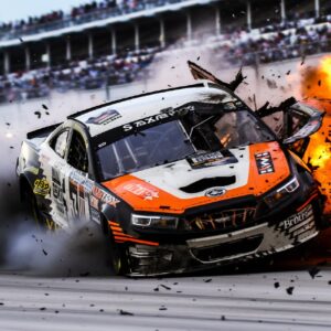 an orange, black, and white nascar violently crashing at daytona speedwayby bigm...