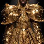 photograph of model wears gold armor dresses and shoes walk the runway on the ru...
